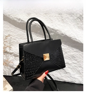 Close-up of black crocodile pattern handbag with golden buckle and top handle