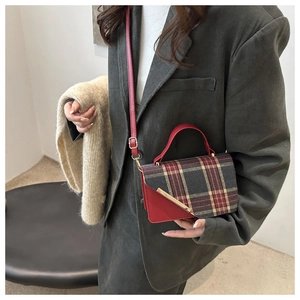 Detail view of red plaid crossbody bag with gold metal trim on green corduroy blazer