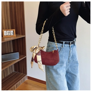 Detail of burgundy suede half-moon bag featuring a thick gold chain and floral silk scarf