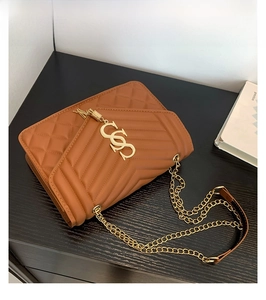 Detailed view of brown quilted crossbody bag with gold chain strap and metal logo hardware