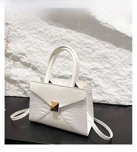 Close-up of white faux leather bag with crocodile pattern and gold square stud lock