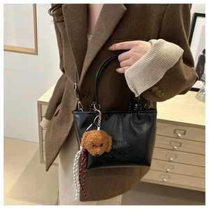 Close-up of black PU leather bucket bag with letter embossing and cute teddy bear pendant
