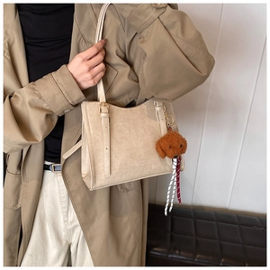 Dettaglio della borsa tote beige con trama in pelle retrò e ciondolo a forma di orsetto