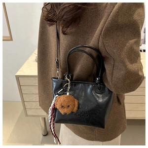 Detail view of black leather bucket bag with embossed text and plush puppy charm pendant