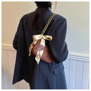 Brown suede underarm bag detail featuring a thick gold chain and a vintage printed scarf