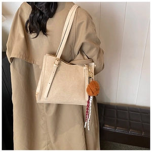 Dettaglio di una borsa tote beige con ciondolo in peluche e trama in pelle