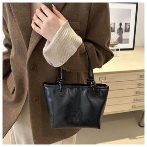 Detail of black leather tote bag featuring knotted handle and embossed letter design