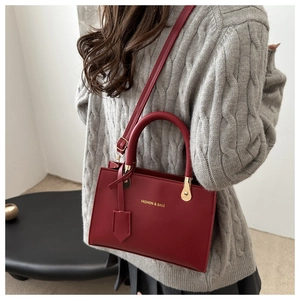 Detail of dark red leather tote bag with gold hardware worn over a grey knit sweater