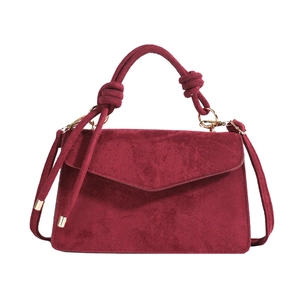 Minimalist burgundy suede handbag with knotted handle and gold metal detail on white background