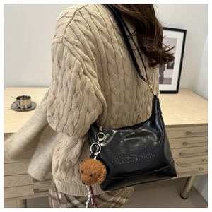 Close-up of black matte leather bag with embossed logo and brown teddy bear plush charm