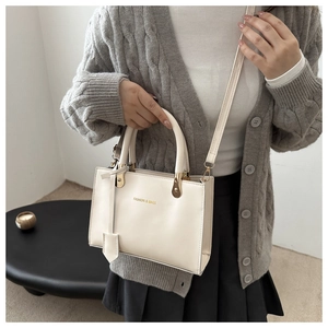 Detail of cream white leather square tote bag with gold lettering and adjustable strap