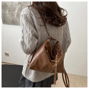 Detail of brown faux leather tote with tassels on a model in grey knit sweater