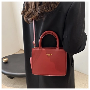 Detail of red square tote bag with gold logo on black blazer with adjustable strap