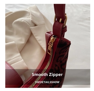 Detail view of smooth golden zipper and leopard print contrast on dark red crescent bag