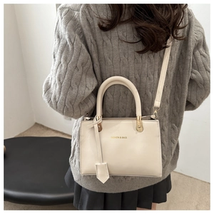 Detail showing the creamy white leather handbag with gold hardware and fashion lettering
