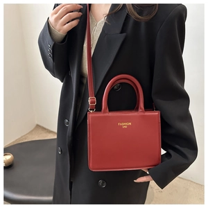 Detailed view of red leather square tote bag with gold lettering and adjustable strap