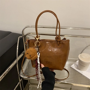 Retro brown PU leather tote bag with dog plush charm and embossed text on a metal shelf