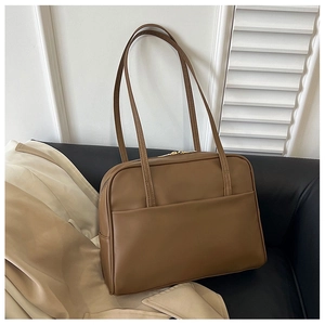 Détail d'un sac cabas marron en cuir avec poche avant et double bandoulière sur canapé