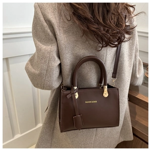 Brown retro box bag with gold lettering shown on model in beige blazer coat