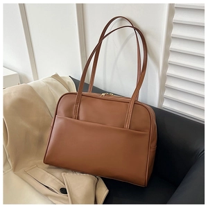 Détail d'un sac cabas en cuir marron avec bandoulières et poche avant sur canapé