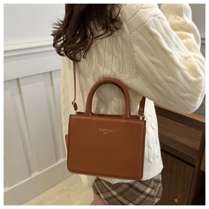 Detailed view of brown leather handbag with gold lettering and adjustable shoulder strap