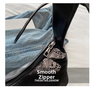 Close-up of smooth silver metal zipper and silver butterfly print on black handbag