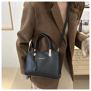 Detail of black leather tote bag with gold metal handle rings and detachable shoulder strap