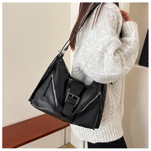 Detail of black faux leather tote bag showing metallic buckles and multiple zipper accents