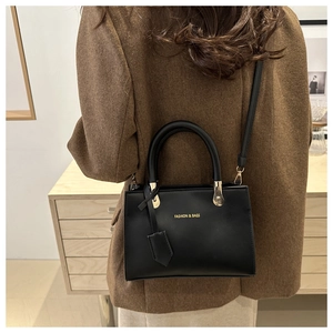 Model wearing a black crossbody square bag with gold hardware and logo detail