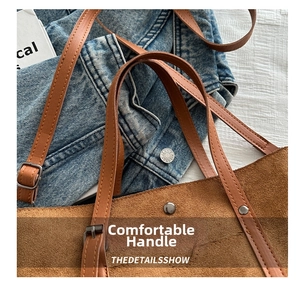 Detail of brown suede tote bag featuring leather handles and decorative metal rivets
