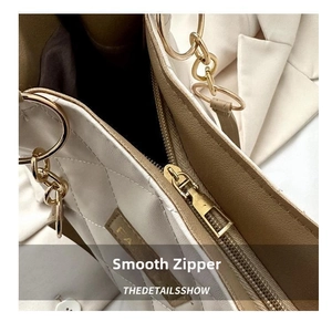 Macro shot of smooth gold zipper and white quilted faux leather texture of tote bag