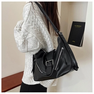 Model wearing a large black matte leather tote bag with double zipper and buckle accents