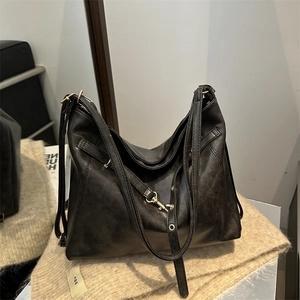 Minimalist black faux leather tote bag with gold hardware on a cozy knit background