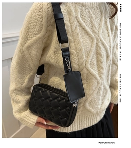 Detail of black quilted shoulder bag with detachable mini pouch and woven strap on model