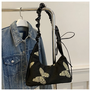 Detail of golden butterfly embroidery on black fabric with ruched leather shoulder strap