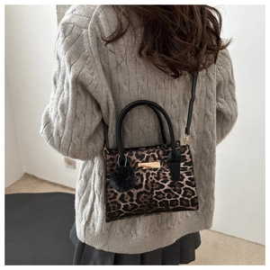 Détail du sac léopard avec plaque dorée et pompon noir, porté avec un pull en maille