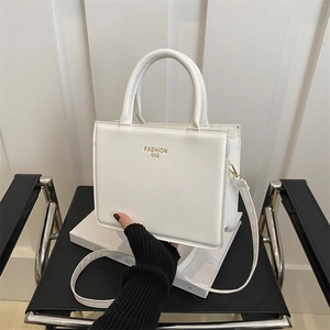Minimalist white square leather tote bag with gold FASHION BAG text on a black chair