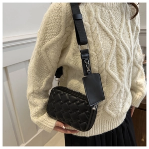 Detail of black quilted crossbody bag with small coin purse on wide woven strap