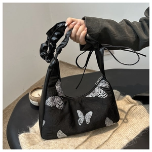 Detail of butterfly embroidery and scrunchie leather handle on a black canvas bag