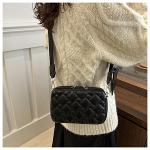 Close-up of black quilted crossbody camera bag with wide strap and mini coin purse detail