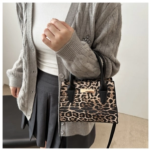 Détail d'un sac à main léopard élégant avec barre métallique dorée et lanières en cuir noir