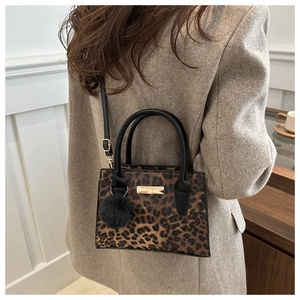 Detail of leopard print crossbody bag featuring black round handles and pompom charm
