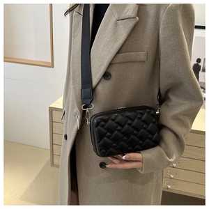 Detail of black quilted crossbody bag with wide canvas strap and silver hardware