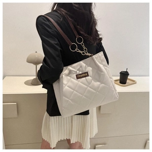 Detail of beige quilted tote bag featuring brown straps and elegant gold chain accents