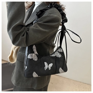 Detail of black underarm bag featuring silver butterfly embroidery and ruffled strap