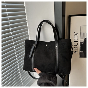 Detail of black suede tote bag showing leather strap and metallic buckle under soft light