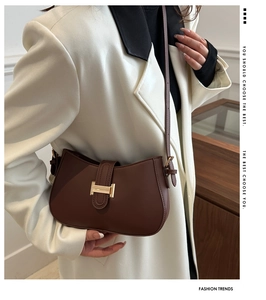 Chic brown underarm bag with gold H-buckle worn by model in elegant white blazer