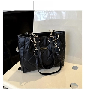 Detail of black quilted tote bag with gold chain strap and metal fashion plate