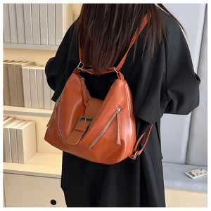 Detail view of vintage brown leather backpack with metallic zippers and decorative buckle