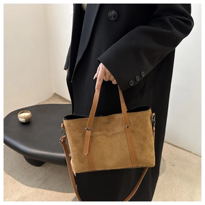 Close-up of brown suede tote bag with metal rivets and adjustable shoulder strap detail